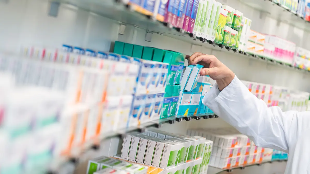 Eine Apothekerin greift in ein Medikamenten-Regal
