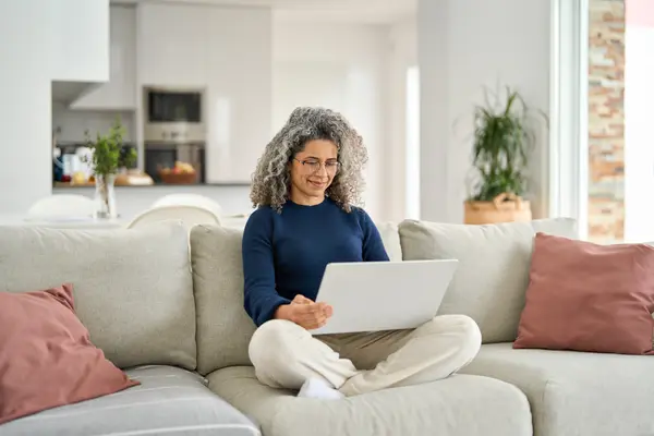 Eine Frau sitzt im Schneidersitz auf einem Sofa mit dem Laptop auf dem Schoß