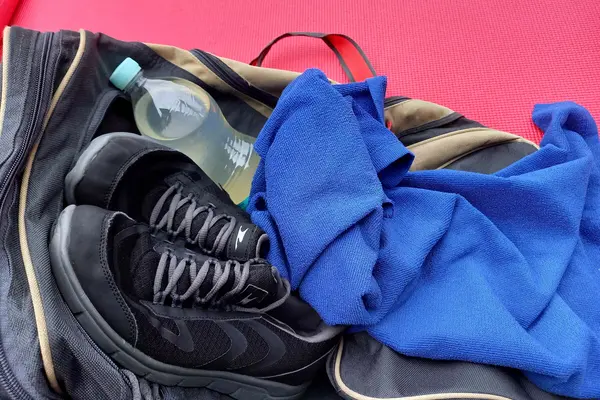 Eine Flasche mit einem Sportgetränk liegt auf einer Trainingstasche, daneben Turnschuhe und ein Handtuch