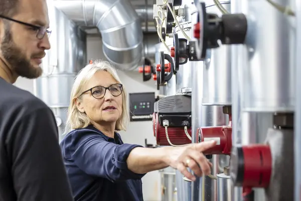 Eine Energieberaterin erläutert einem Verbraucher eine technische Anlage im Keller.