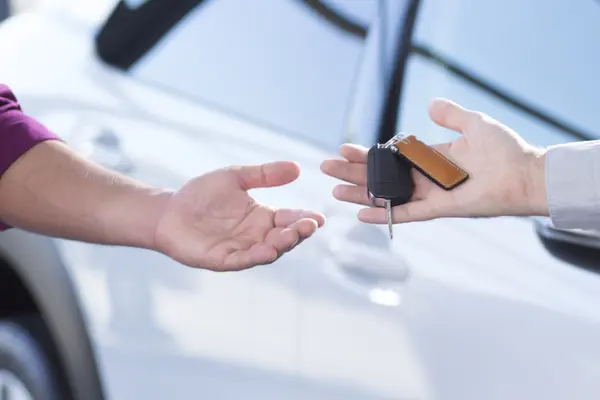 In der Nahaufnahme von zwei Händen übergibt ein Mann einer Frau einen Autoschlüssel