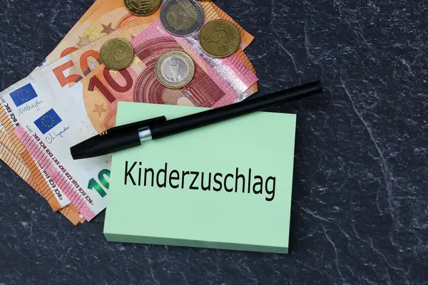 Zettel, auf dem das Wort Kinderzuschlag steht, ein Kugelschreiber sowie Geldscheine und Münzen