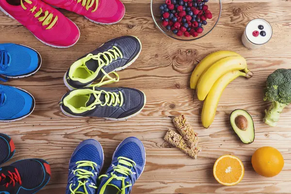mehrere Paare Turnschuhe stehen vor Bananen, Avocado, Müsliriegeln und anderen Lebensmitteln