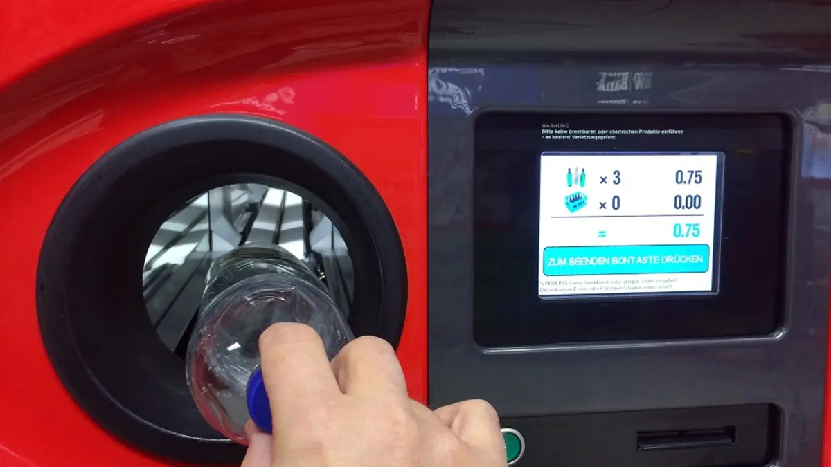 Eine Hand schiebt eine Flasche in einen Leergutautomaten.