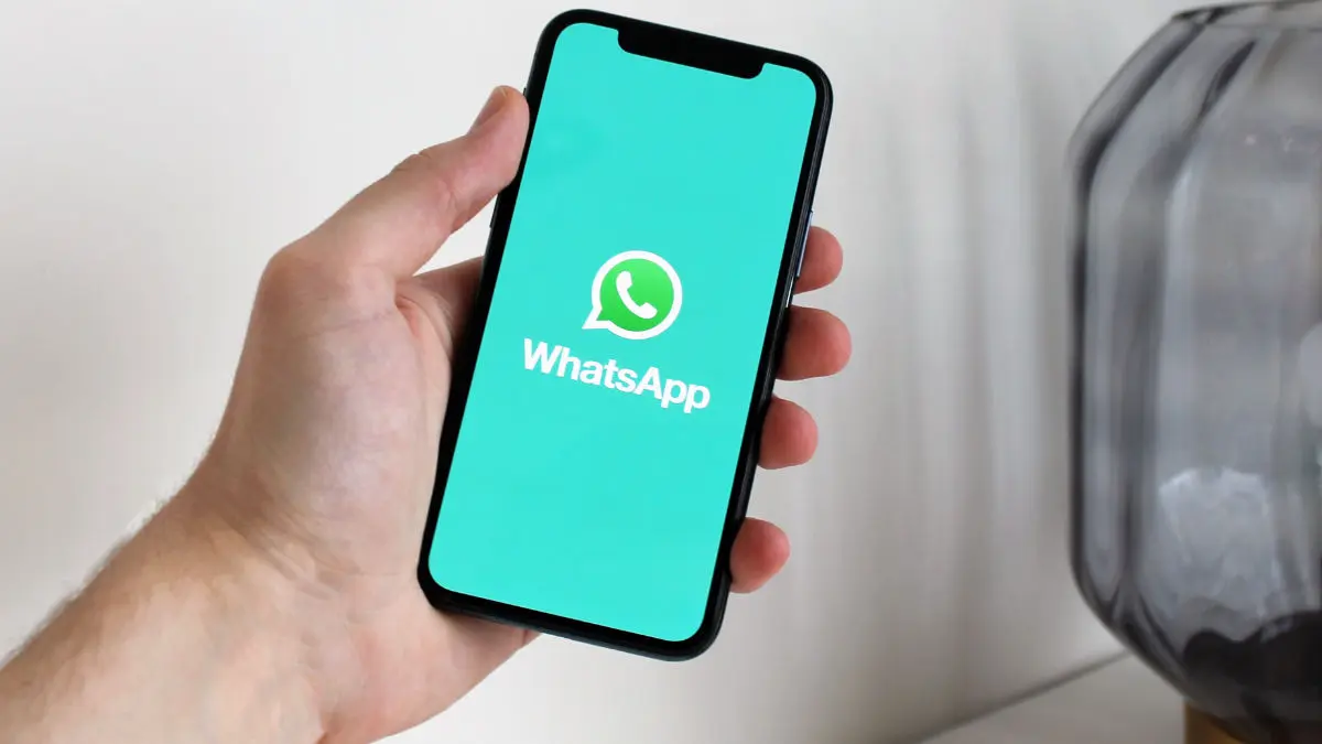 Eine Hand hält ein Smartphone, dessen Display das Logo von WhatsApp und die Schrift "WhatsApp" zeigt.