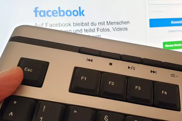Daumen auf ESC-Taste einer Tastatur vor dem Login-Bildschirm von Facebook