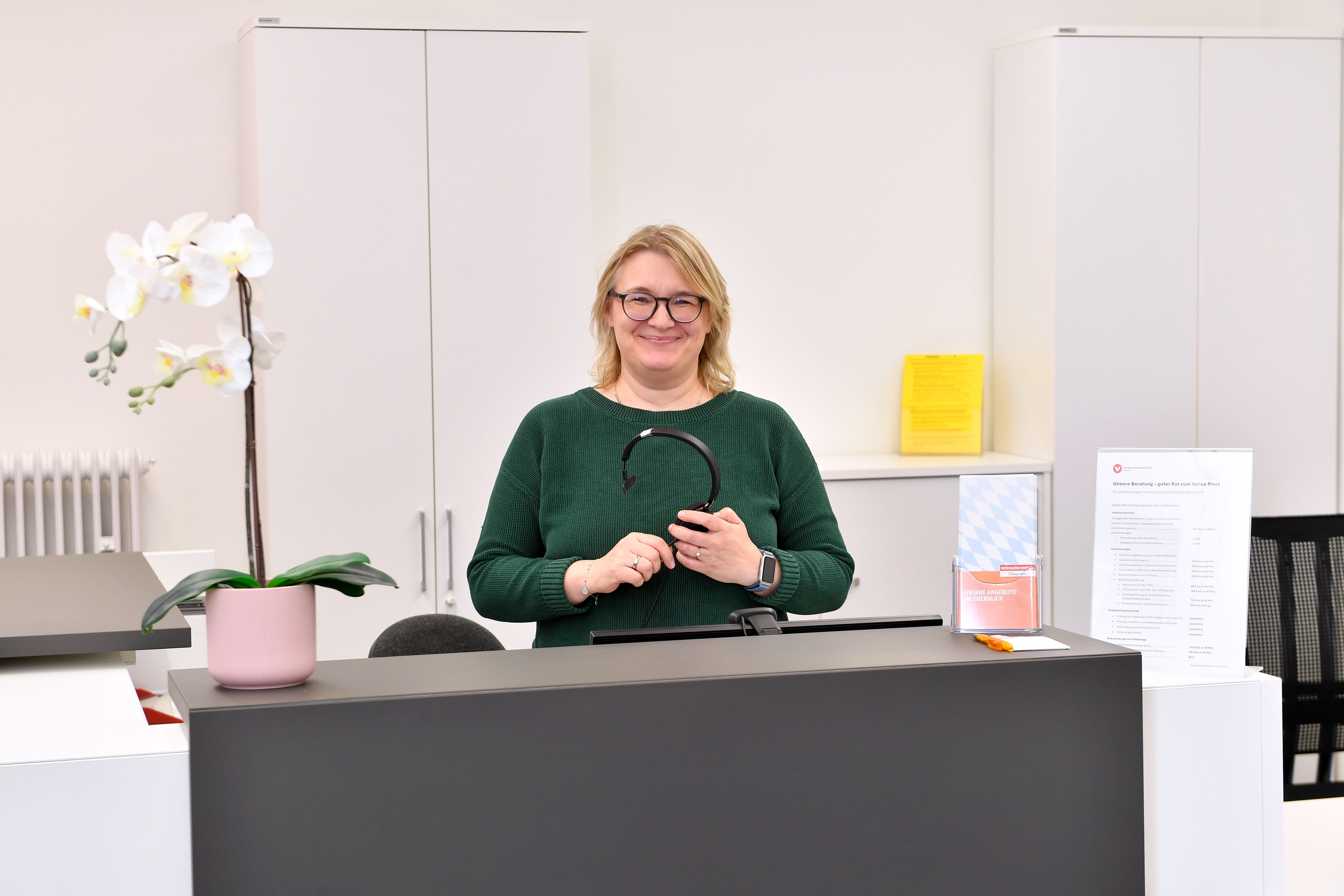 Eine Frau steht hinter einem Empfangstresen und lächelt in die Kamera