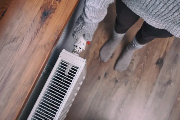 Frau mit Handschuh dreht an Thermostat der Heizung