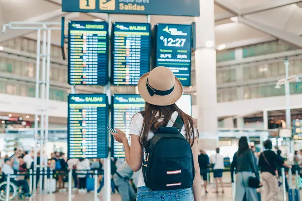 Frau steht am Flughafen und schaut auf Anzeigetafel