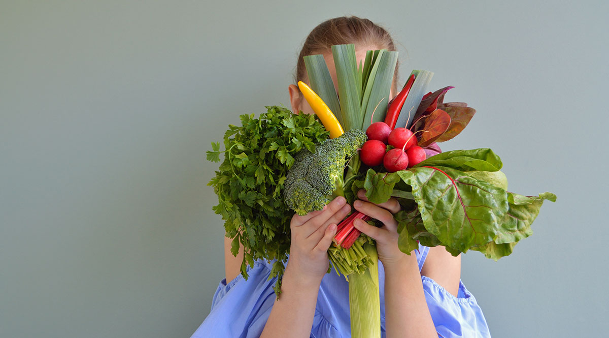 Eine Frau hält einen Strauß aus Gemüse vor ihr Gesicht 