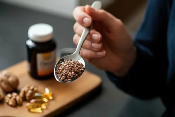 Hand hält Löffel mit Leinsamen in der Nähe von Nahrungsergänzungsmitteln