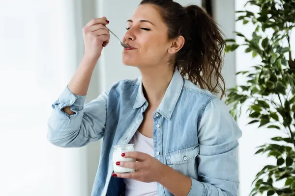 junge Frau löffelt genüsslich einen Joghurt aus einem Plastikbecher