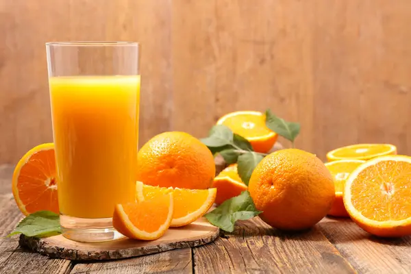 Ein Glas Orangensaft steht auf einem Tisch. Daneben liegen aufgeschnittene und ganze Orangen.