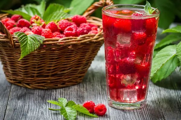 Neben einem Korb mit Himbeeren steht ein Glas mit Himbeer-Shrub