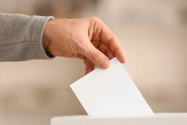 Hand mit Wahlzettel, der in Urne eingeworfen wird