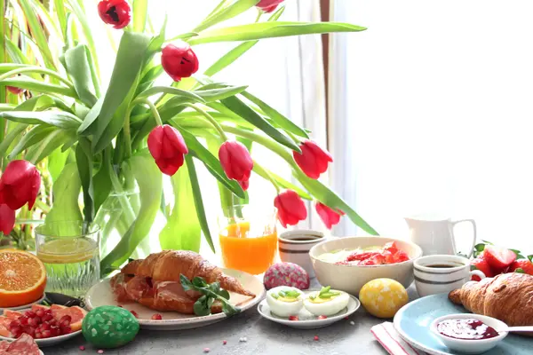 Osterfrühstück mit bunten Eiern und roten Tulpen