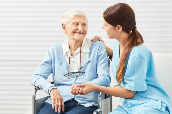 Pflegerin kümmert sich um Seniorin im Rollstuhl