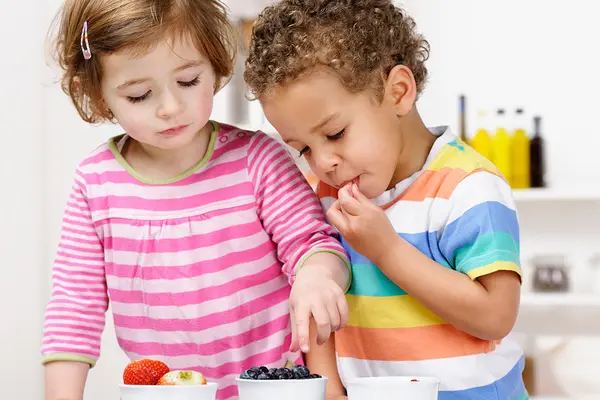 Kleines Mädchen und kleiner Junge essen verschiedene Obstsorten aus Schälchen
