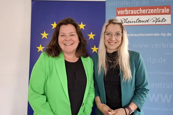 Zwei Frauen vor einem Banner mit der Europa-Flagge und lächeln in die Kamera.