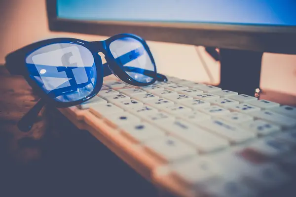 Auf einer Computertastatur liegt eine Brille, in der sich das Facebook-Logo spiegelt.