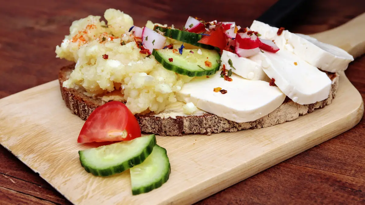 ein belegtes Brot mit Käse, Gurke und Tomate auf einem Brettchen