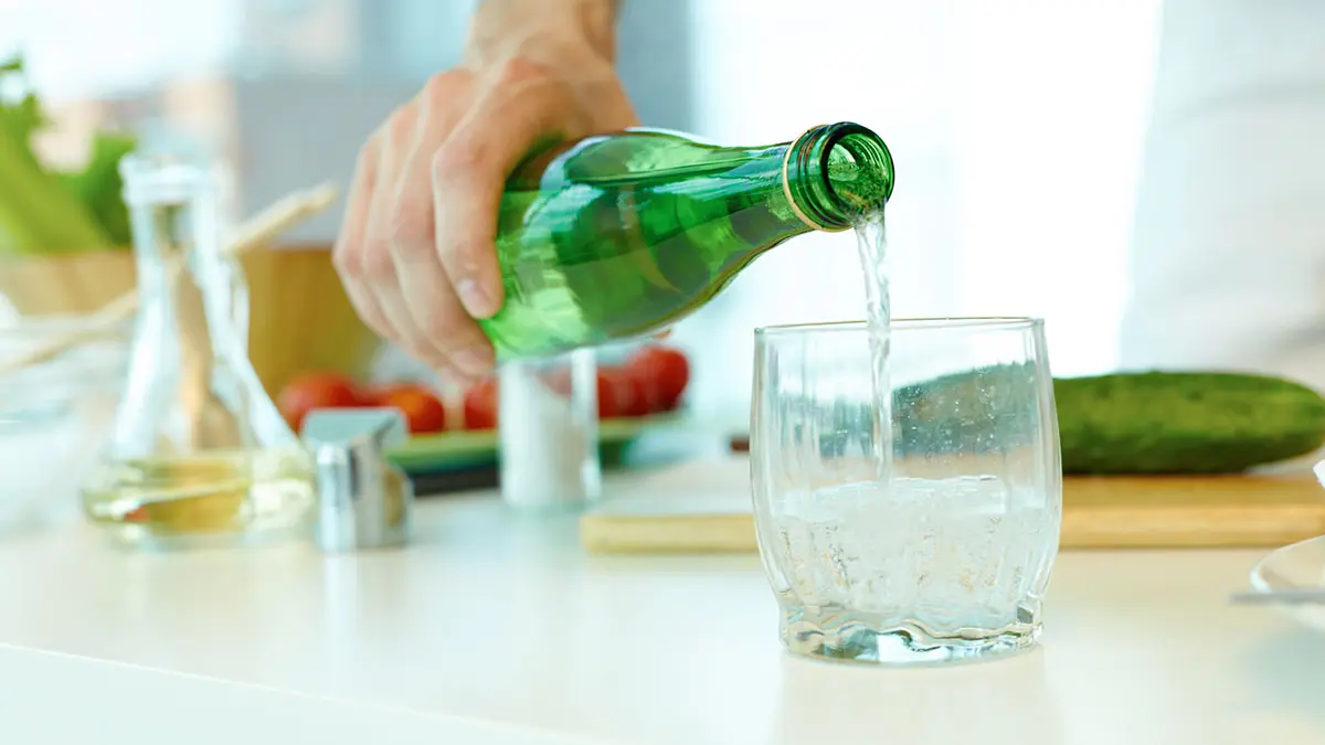 Jemand gießt Wasser aus einer grünen Mehrweg-Flasche in ein Glas