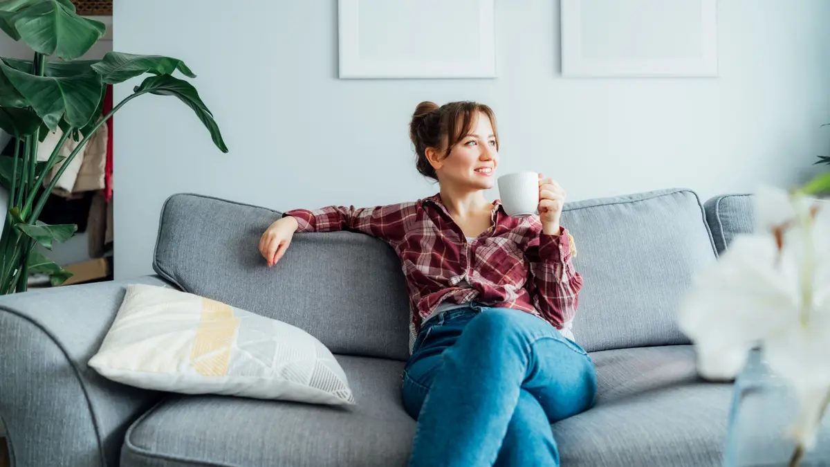 Eine Frau sitz entspannt mit einer Tasse in der Hand auf dem Sofa