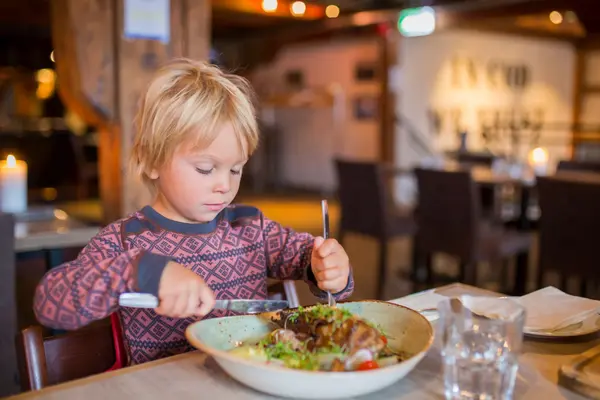 Ein Kind in einem Restaurant isst mit Messer und Gabel.