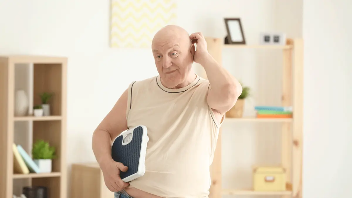 Ein Senior mit der Waage unter dem Arm. Soll er abnehmen?