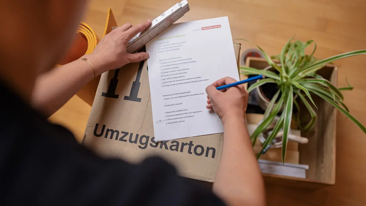 Mann hakt Umzugs-Checkliste auf Umzugskarton ab