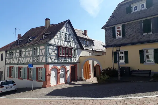 Zwei ältere Häuser an einer gepflasterten Straße.