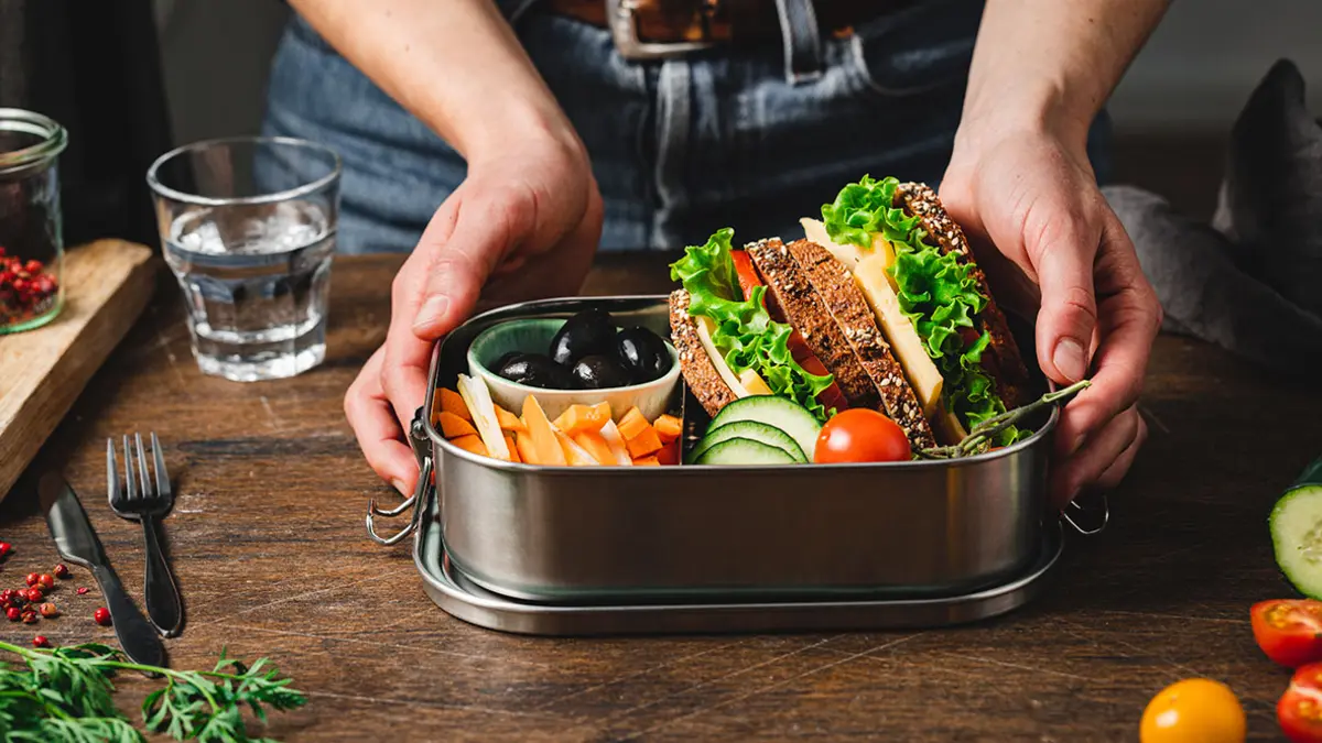 Jemand bereitet eine Lunchbox mit Broten, Obst und Gemüse zu