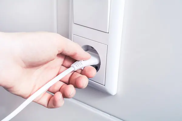 Hand steckt einen Stecker in eine Steckdose