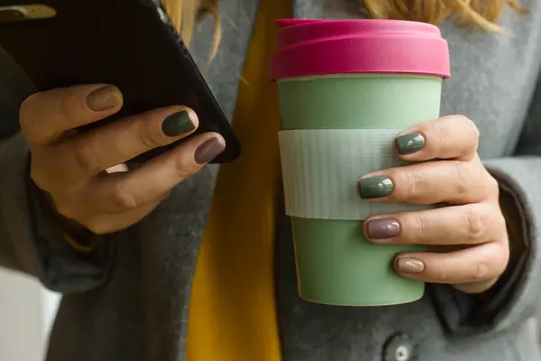 Junge Frau hält wiederverwertbaren Kaffeebecher in einer Hand