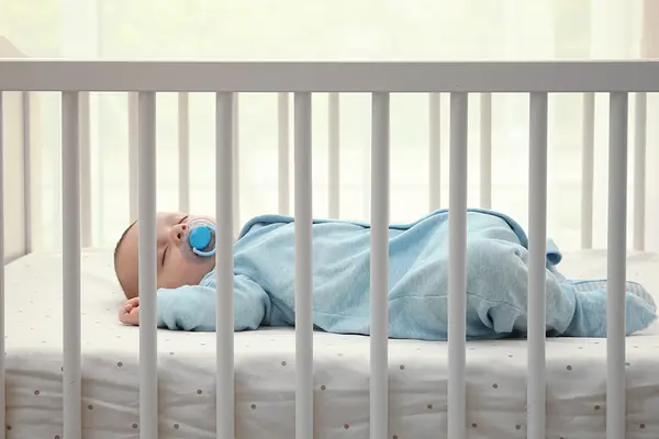 Baby in blauem Strampler schläft in weißem Bett