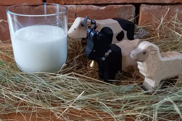 Kuh, Schaf und Ziege als Holzfiguren stehen neben einem Glas Milch.