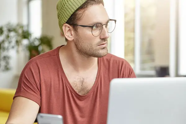 Ein Mann sitzt genervt vor seinem Laptop und schaut zur Seite 