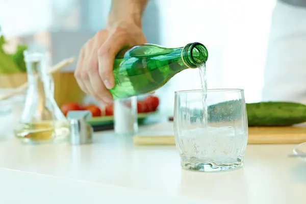 Jemand gießt Wasser aus einer grünen Mehrweg-Flasche in ein Glas