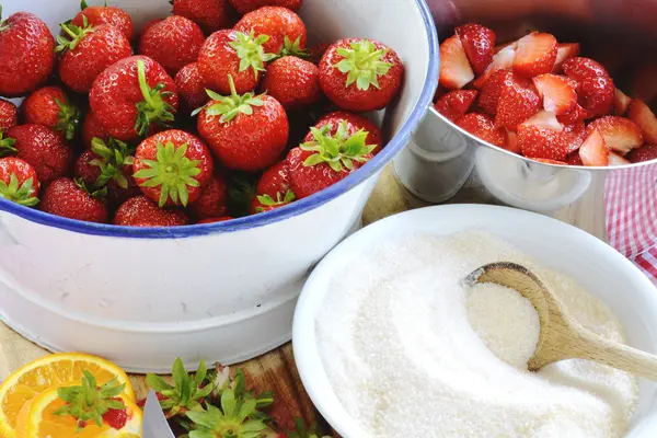 Viele Erdbeeren neben Töpfen, Zucker und weiteren Küchenuntensilien.