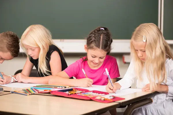 Drei Grundschulkinder sitzen an einem Schultisch und lernen