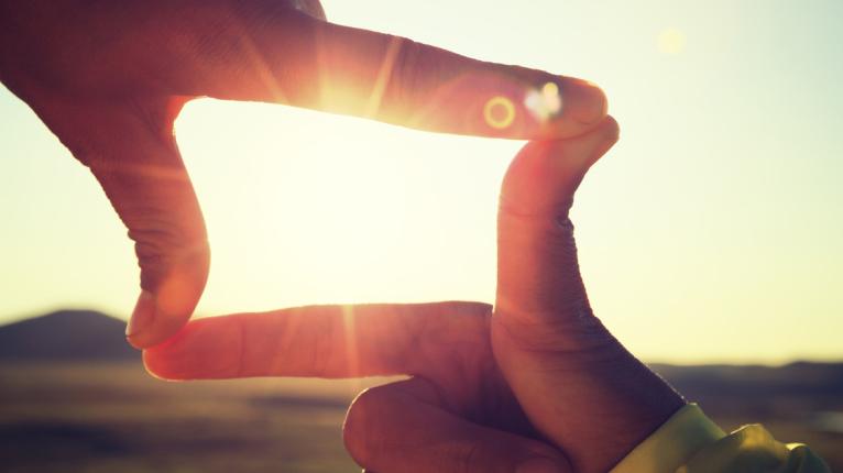 Bild mit Händen, die die Sonne einrahmen.