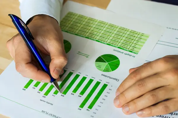 Männerhände auf einem Blatt mit grünen Diagrammen, eine Hand hält einen Stift