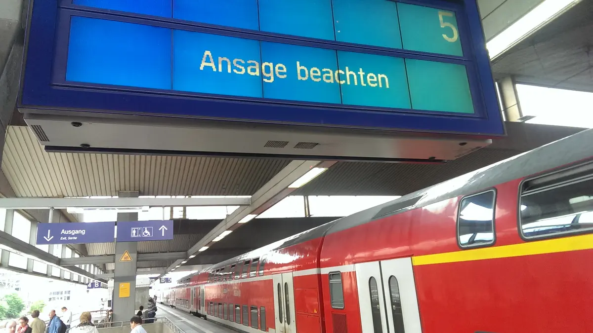 Ein doppelstöckiger Regionalzug steht an einem Bahnhofsgleis, auf der Anzeige steht: "Ansage beachten"