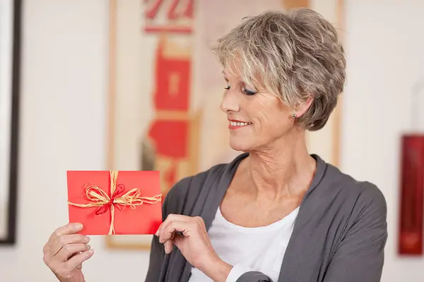 ältere Frau hält einen Geschenkgutschein und lächelt