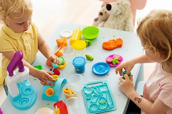 Zwei Kleinkinder basteln am Tisch mit farbiger Knete