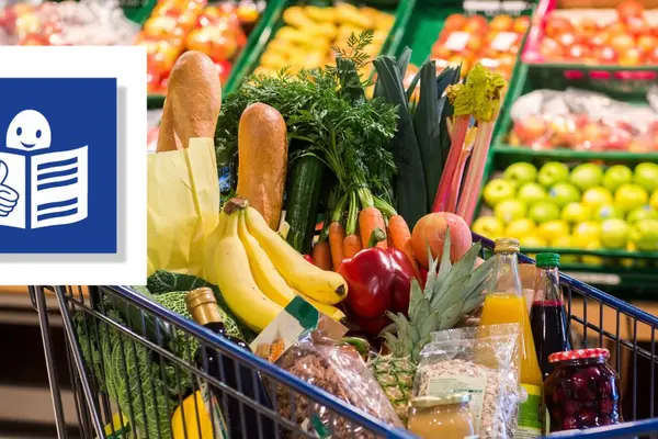 es sind Supermarkt-regale gfüllt mit Obst und Gemüse auf dem Bild. Davor steht ein Einkaufswagen. In dem Einkaufwagen sind Bananen und andere gesunde Lebensmittel.
