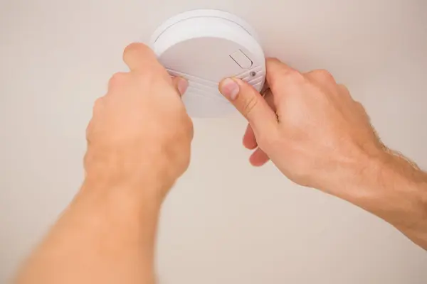 Zwei Hände arbeiten an einem Rauchmelder an der Decke