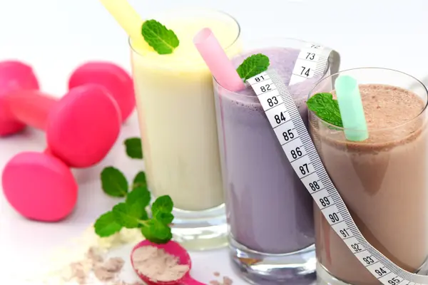 Drei Gläser mit Eiweißshakes stehen nebeneinander, daneben liegen Hanteln.