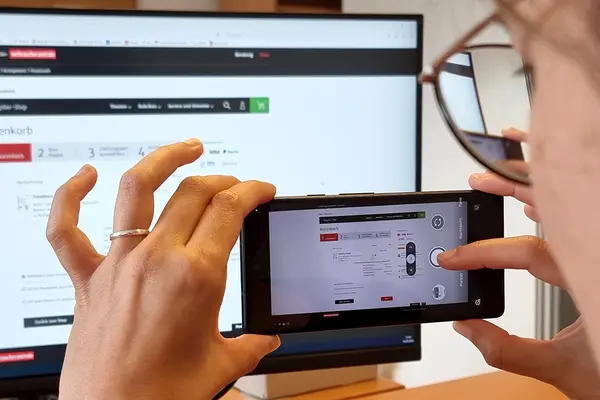 Eine Frau richtet Smartphone auf einen Monitor, um ihn zu fotografieren
