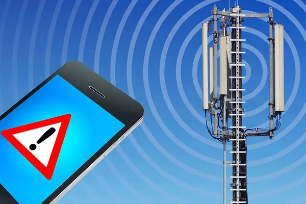 Smartphone mit Achtung-Symbol auf dem Display neben Mobilfunkmast